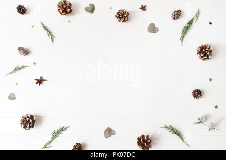 Weihnachten dekorative Komposition. Floral frame der immergrünen Blätter juniperus Zweige, Eukalyptus, Kiefer, Lärche, Kegel und glitzerndes Konfetti Sterne. Weiße Holztisch Hintergrund. Botanische Muster. Stockfoto