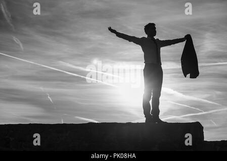 Geschäftsmann im Anzug mit Hintergrundbeleuchtung durch eine Sunburst bei Sonnenaufgang, als er mit ausgestrecktem Arm an der Wand steht. Stockfoto