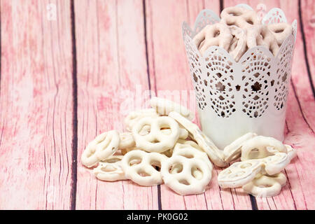 Schönen leckeren Joghurt abgedeckt Brezeln in Vanille und Himbeere Geschmack. Einige in einem Eimer. Rosa Holz Hintergrund Stockfoto