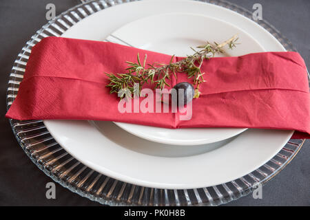 Ein Mittagstisch mit unter Teller Set, schöne graue und weiße Platten, rot Serviette, kleine dekorative tree branch, zwei Trauben mit Blumen und Obst Dekor Stockfoto