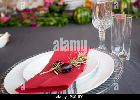 Ein Mittagstisch mit unter Teller Set, schöne graue und weiße Platten, rot Serviette, kleine dekorative tree branch, zwei Trauben mit Blumen und Obst Dekor. Stockfoto