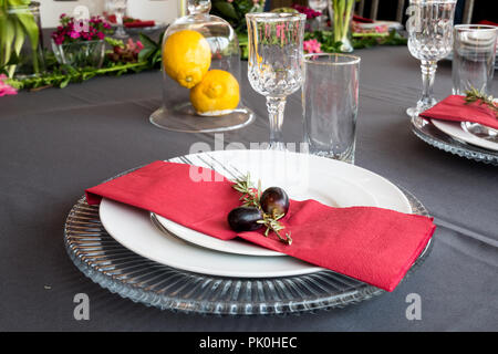 Ein Mittagstisch mit unter Teller Set, schöne graue und weiße Platten, rot Serviette, kleine dekorative tree branch, zwei Trauben mit Blumen und Obst Dekor. Stockfoto