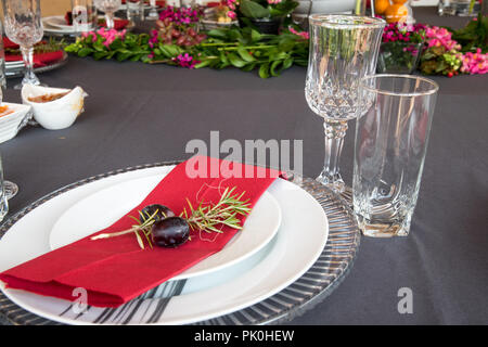 Ein Mittagstisch mit unter Teller Set, schöne graue und weiße Platten, rot Serviette, kleine dekorative tree branch, zwei Trauben mit Blumen und Obst Dekor. Stockfoto