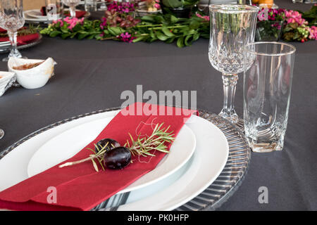 Ein Mittagstisch mit unter Teller Set, schöne graue und weiße Platten, rot Serviette, kleine dekorative tree branch, zwei Trauben mit Blumen und Obst Dekor. Stockfoto