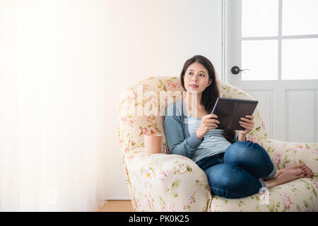 Aisan Junge hübsche Mädchen zu Hause chillen und sitzt auf einem gemütlichen Sofa im Wohnzimmer, während Sie Tablet. Stockfoto