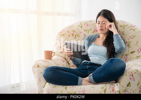 Junge Frau müde, während auf Tablet sitzen auf der Couch in Urlaub zu Hause lesen. Stockfoto