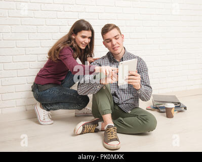 Junge und Mädchen Schüler sitzen auf dem Boden gegen eine Mauer mit einem Tablet Stockfoto