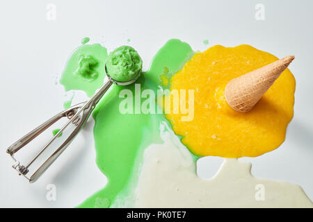 Bunte Spritzer von geschmolzenem Eis. Schaufel von grünem Eis und einem gefallenen Waffel Kegel mit einem gelben Eis auf einen Schnitzer Hintergrund mit einem Co Stockfoto
