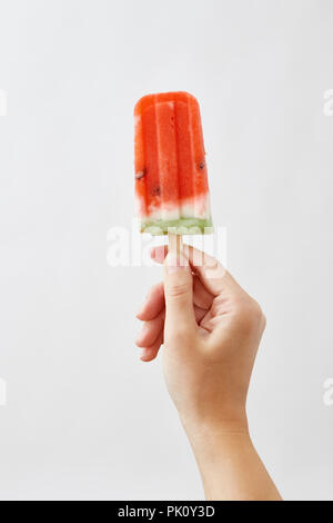 Die Hände eines Mädchens Holding appetitlich, frische Scheiben Wassermelone auf einem Stock auf einem weißen Hintergrund. Das Konzept der gesunden hausgemachtes Eis Popsicle mit Spa Stockfoto