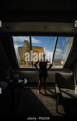 Eine Frau schaut aus einem Hotel Zimmer im Luxor Hotel und Casino in Richtung Mandalay Bay und Delano Resorts in Las Vegas, Nevada, USA. Stockfoto