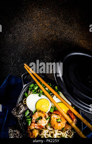 Traditionelle asiatische Lebensmittel, Ramen Suppe mit Garnelen, Nudeln, Frühlingszwiebel, in Scheiben geschnittene Eier, Pilze, auf dunklen konkreten Hintergrund mit Stäbchen Platz kopieren Stockfoto