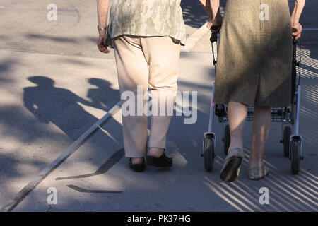 Zwei alte Frauen von der Rückseite aus betrachtet, Schatten auf der Straße, langsam zu Fuß mit einer Gehhilfe, iconic Foto Stockfoto