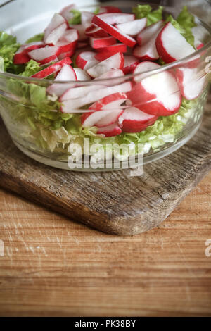 Pflanzliche vegan Bärlauch Salat, Radieschen, Frühlingszwiebeln, Kohl und Salat in einer großen durchsichtigen Teller auf einem antiken Holz- Hintergrund. Close-up Stockfoto