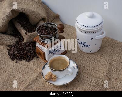 Alte Kaffeemühle mit einer Tasse Kaffee, Kaffeebohnen in einem Sack und der Kaffee kann von oben gesehen Stockfoto