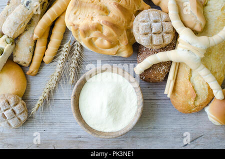Verschiedene Arten von traditionellen Italienischen frisch gebackenes Brot und Brötchen mit Schüssel Mehl auf hölzernen Tisch Hintergrund. Rustikale Vintage Style. Ansicht von oben. Stockfoto