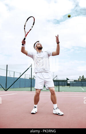 Profi-Tennisspieler tut ein Kick-Tennis auf dem Tennisplatz an einem sonnigen Sommermorgen. Das ist in der Sportswear gekleidet. Stockfoto