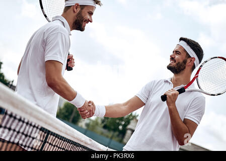 Zwei Männer, professionelle Tennisspieler schütteln sich die Hände vor und nach dem Tennis Match. Einer der Sie angesichts der Wut hat. Er versucht, seine Gegner einzuschüchtern. Stockfoto