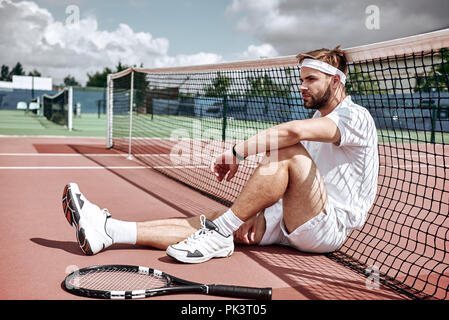 Entspannung nach gutes Spiel. Freundliche Mann am Tennis net ruhend sitzen auf Tennisplatz Stockfoto