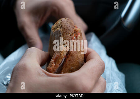 Nahaufnahme eines jungen kaukasischen Mann essen einen Schinken und Käse Sandwich, aus einer Plastiktüte, sitzen auf dem Fahrersitz eines Autos Stockfoto
