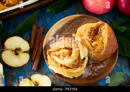 Frische, hausgemachte Brötchen Brötchen mit Äpfeln und Zimt in Glasur close-up auf einem blauen vintage Holz- Hintergrund. Stockfoto