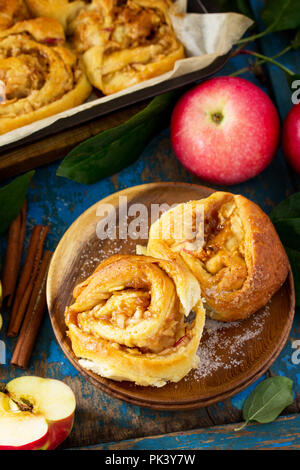 Frische, hausgemachte Brötchen Brötchen mit Äpfeln und Zimt in Glasur auf einem blauen vintage Holz- Hintergrund. Stockfoto