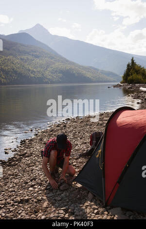 Mann einrichten Zelt in der Nähe des Riverside Stockfoto