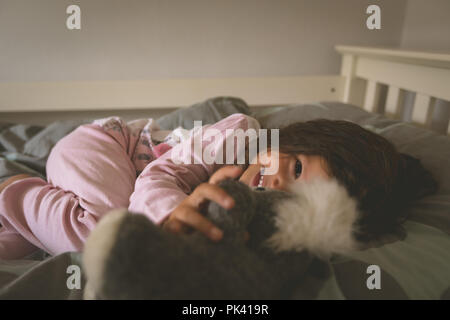 Mädchen spielen mit Teddybär auf Bett Stockfoto
