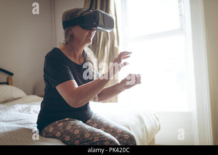 Ältere Frau mit Virtual reality Headset im Schlafzimmer Stockfoto