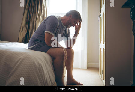 Älterer Mann sitzt auf dem Bett im Schlafzimmer zu Hause Stockfoto