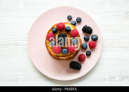 Pfannkuchen mit Beeren auf einem rosa Platte auf weißem Holz- Tabelle, Ansicht von oben. Von oben, Ansicht von oben. Stockfoto