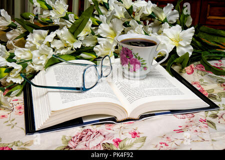 Buchen Sie öffnete mit Brille und eine Tasse Kaffee neben ihn beim Lesen. Blumenstrauß im Bild. Stockfoto