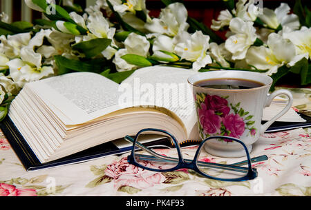 Buchen Sie öffnete mit Brille und eine Tasse Kaffee neben ihn beim Lesen. Blumenstrauß im Bild. Stockfoto