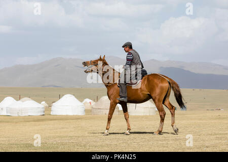 Song Kul, Kirgistan, 8. August 2018: einem Kirgisischen reitet ein Pferd, das Pfeifen ist durch die Steppe bei Song Kul See in Kirgisistan Stockfoto