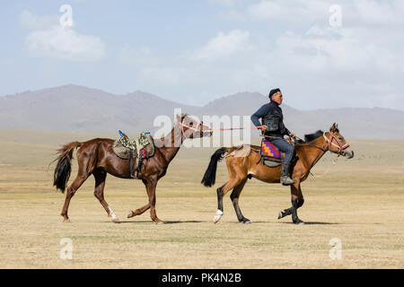 Song Kul, Kirgistan, 8. August 2018: einem Kirgisischen reitet sein Pferd und führt ein weiteres an der Leine Song Kul See in Kirgisistan Stockfoto