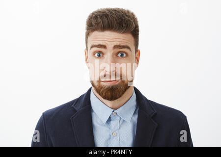 Taille - geschossen von albern und düsteren cute brunet Freund mit blauen Augen und Bart grinsend stehen im eleganten Anzug Gefühl es tut uns Leid entschuldigen, der als dumm posiert vor grauem Hintergrund Stockfoto