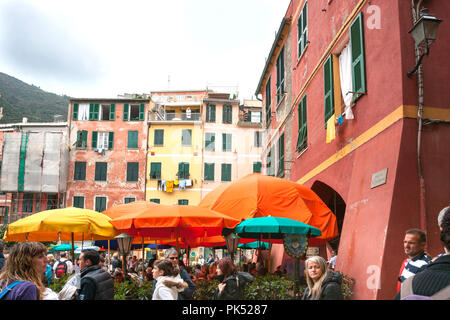 MONTEROSSO ITALIEN - 24. APRIL 2011; Masse von Touristen unter hellen Sonnenschirmen in der Stadt Piazza G Marconi von Apartment Gebäuden umgeben Stockfoto