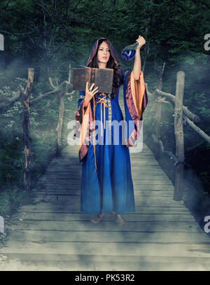 Schöne junge Halloween Hexe Vintage gothic Kleid mit Kapuze magische Buch von Zaubersprüchen in alten Lederbezug und trank in Glas halten Stockfoto