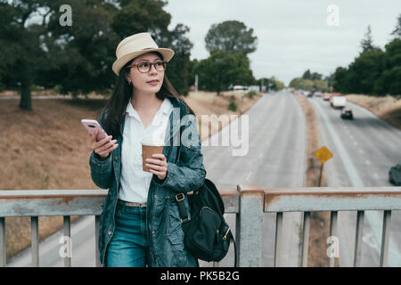 Schöne Frau mit Kaffee und Telefon und lehnte sich auf die Leitplanke auf der Brücke mit Freuden. Stockfoto