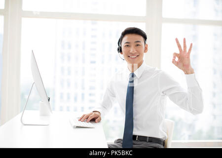 Fröhlicher junger Unternehmer arbeiten im Büro mit Headset Stockfoto