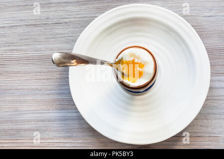 Blick von oben auf die weich gekochten braunen Ei mit Löffel in der Tasse auf weiße Platte auf grau Holzbrett mit leeren copyspace Stockfoto