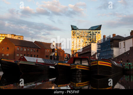 Birmingham, England. Bild des Kanals mit dem Cube Gebäude im Hintergrund bei Sonnenuntergang. Niedrigen Winkel aus neben dem Kanal der Boote in das Becken. Stockfoto