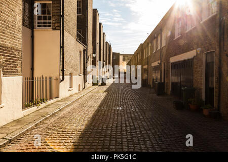 Gepflasterte Straße in London im hellen Sonnenschein. Dieses London Mews Zurück Zu viktorianischen Zeiten hat das ursprüngliche Kopfsteinpflaster mit einem steilen Sturz. Stockfoto