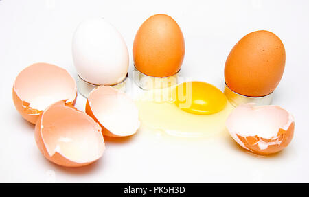 Konzept Bild der braune und weiße Eier zusammen mit gebrochenen Eierschalen und Eigelb auf weißem Hintergrund verschüttet. Stockfoto