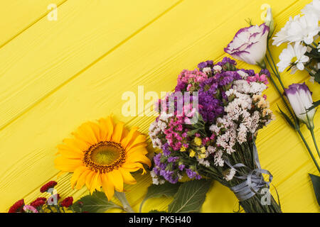 Vielzahl von Blumen auf Holz. Dahlie, Sonnenblumen, getrocknete statice Limonium, Lisianthus und Kamillenblüten. Gelb Holz- Hintergrund. Stockfoto