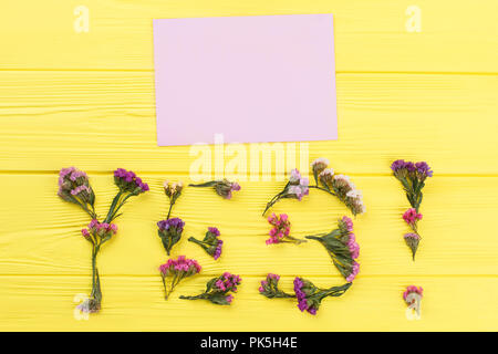 Wort ja aus statice Blumen und leeres Papier für Copyspace. Gelbe Holztisch Oberfläche Hintergrund. Stockfoto