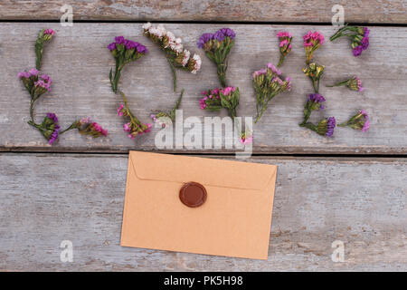 Liebe Wort aus statice Blumen und Umschlag mit Wachs. Ansicht von oben. Alte vintage Schreibtisch aus Holz Oberfläche Hintergrund. Stockfoto