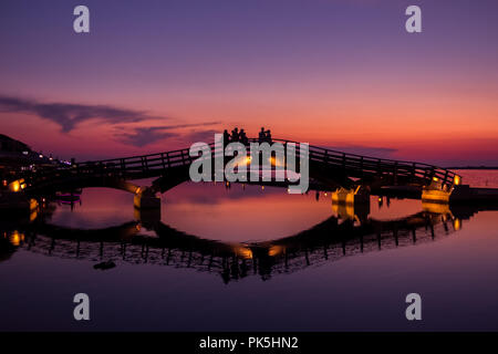 Silhouetten und Reflexionen bei Touristen, die einen wunderschönen Sonnenuntergang über der Marina-Brücke in Lefkada (Lefkas), Griechenland, genießen Stockfoto