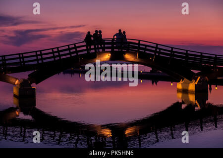 Silhouetten und Reflexionen bei Touristen, die einen wunderschönen Sonnenuntergang über der Marina-Brücke in Lefkada (Lefkas), Griechenland, genießen Stockfoto