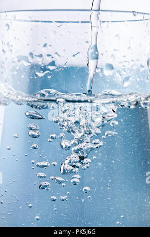 Aktion Close up (Makro) schoß auf klaren blauen Wasser in ein Glas mit Sauerstoff Blasen bilden und steigende gegossen wird. Stockfoto