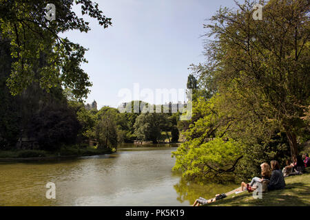 Die Menschen genießen Sie sonnige Wetter an einem See im Park (Parc des Buttes-Chaumont) in Paris. Stockfoto